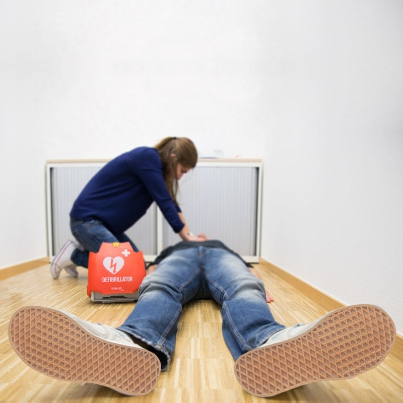 Woman performing CPR with defibrillator on person lying on floor in emergency situation